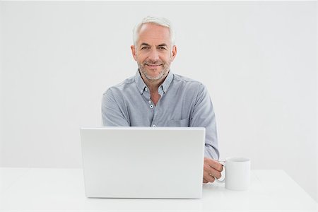 simsearch:400-07230809,k - Portrait of a smiling mature businessman with laptop and coffee cup against white background Foto de stock - Super Valor sin royalties y Suscripción, Código: 400-07230833