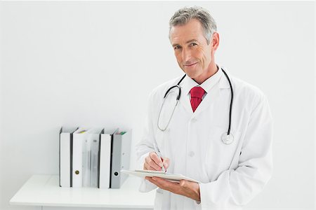 simsearch:614-06898452,k - Portrait of a smiling male doctor writing a report at the medical office Stock Photo - Budget Royalty-Free & Subscription, Code: 400-07230958