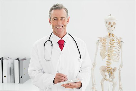 simsearch:614-06898452,k - Portrait of a smiling male doctor writing a report at the medical office Stock Photo - Budget Royalty-Free & Subscription, Code: 400-07230963