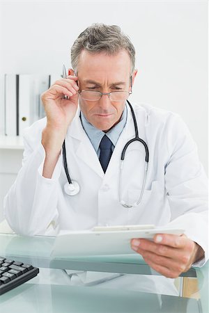 simsearch:614-06898452,k - Serious male doctor reading a report at desk in medical office Stock Photo - Budget Royalty-Free & Subscription, Code: 400-07230996