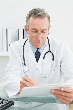 simsearch:614-06898452,k - Serious male doctor writing a report at desk in medical office Stock Photo - Budget Royalty-Free & Subscription, Code: 400-07230997