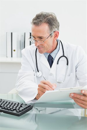 simsearch:614-06898452,k - Concentrated male doctor writing a report at desk in medical office Stock Photo - Budget Royalty-Free & Subscription, Code: 400-07230999