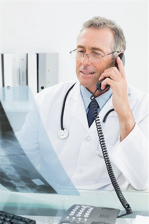 simsearch:400-07269250,k - Male doctor looking at x-ray picture while using the telephone at medical office Stock Photo - Budget Royalty-Free & Subscription, Code: 400-07231005