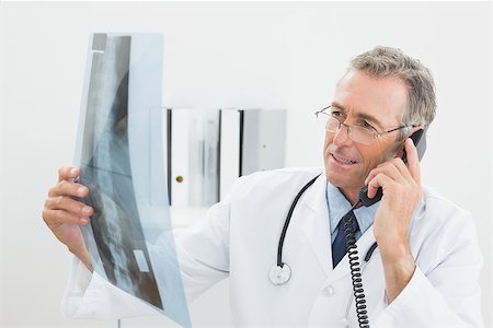 simsearch:400-07269250,k - Male doctor looking at x-ray picture while using the telephone at medical office Stock Photo - Budget Royalty-Free & Subscription, Code: 400-07231006