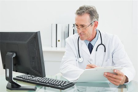 simsearch:614-06898452,k - Concentrated male doctor with report looking at computer monitor at desk in medical office Stock Photo - Budget Royalty-Free & Subscription, Code: 400-07231000