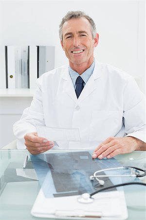 simsearch:614-06898452,k - Portrait of a smiling male doctor sitting at desk in medical office Stock Photo - Budget Royalty-Free & Subscription, Code: 400-07231014