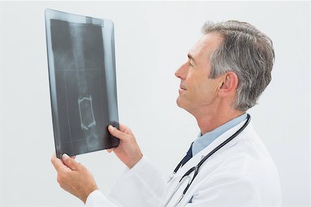 simsearch:400-07269250,k - Side view of a concentrated male doctor looking at x-ray over white background Stock Photo - Budget Royalty-Free & Subscription, Code: 400-07231018