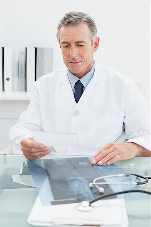 simsearch:614-06898452,k - Serious male doctor reading a note at desk in medical office Stock Photo - Budget Royalty-Free & Subscription, Code: 400-07231012