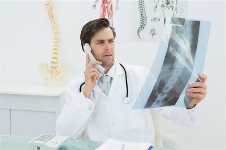 simsearch:400-07269250,k - Male doctor looking at spine x-ray picture while using the telephone at medical office Stock Photo - Budget Royalty-Free & Subscription, Code: 400-07231981