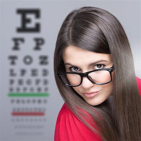 simsearch:400-08407302,k - Beautiful young Caucasian brunette woman taking an eye vision test wearing glasses looking at camera against gray background. Stock Photo - Budget Royalty-Free & Subscription, Code: 400-07246626