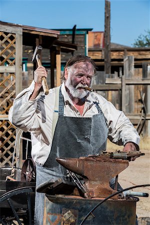 dirty overalls pictures - Male Blacksmith in Old West Swings Hammer at Anvil Stock Photo - Budget Royalty-Free & Subscription, Code: 400-07256636