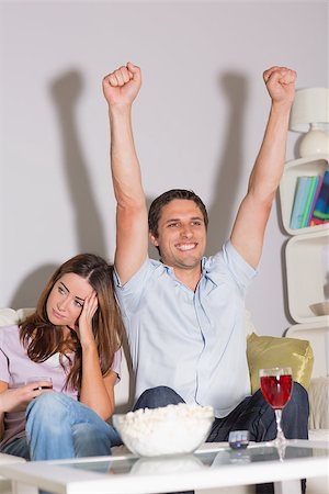 Excited man watching TV with wine glass and popcorn besides a bored woman on sofa at home Stock Photo - Budget Royalty-Free & Subscription, Code: 400-07266791