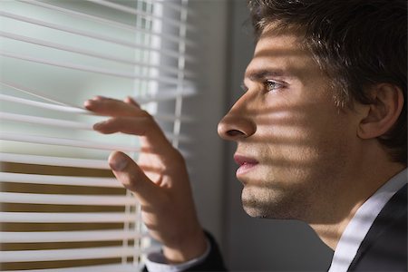 Close-up side view of a serious young businessman peeking through blinds in the office Stock Photo - Budget Royalty-Free & Subscription, Code: 400-07266905