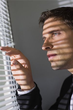 Close-up side view of a serious young businessman peeking through blinds in the office Stock Photo - Budget Royalty-Free & Subscription, Code: 400-07266906