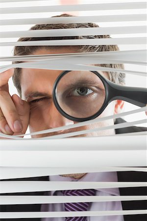 Close-up portrait of a young businessman peeking through blinds with magnifying glass in the office Stock Photo - Budget Royalty-Free & Subscription, Code: 400-07266915