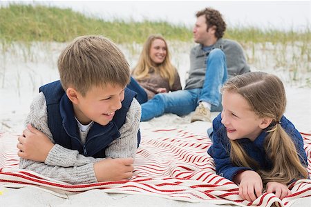 simsearch:400-07267212,k - Happy siblings lying with parents sitting in background at the beach Stockbilder - Microstock & Abonnement, Bildnummer: 400-07267344