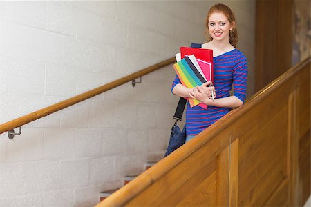 simsearch:400-07267769,k - Redhead student holding folders on the stairs smiling at camera at the university Stock Photo - Budget Royalty-Free & Subscription, Code: 400-07267692