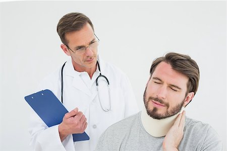 simsearch:400-07269643,k - Male doctor examining a patient's sprained neck over white background Fotografie stock - Microstock e Abbonamento, Codice: 400-07269632