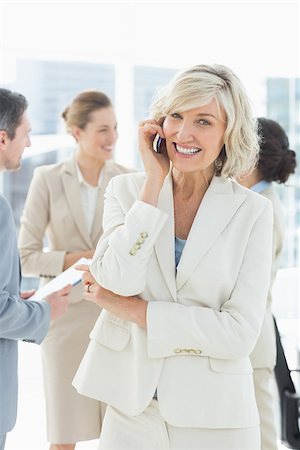 simsearch:400-07274497,k - Portrait of a smiling mature businesswoman on call with colleagues discussing in background at a bright office Stock Photo - Budget Royalty-Free & Subscription, Code: 400-07274477