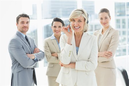 simsearch:400-07274497,k - Portrait of a smiling mature businesswoman wearing headset with colleagues in background at a bright office Stock Photo - Budget Royalty-Free & Subscription, Code: 400-07274480