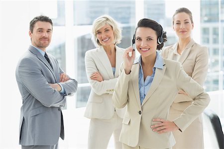 simsearch:400-07274497,k - Portrait of a smiling businesswoman wearing headset with colleagues in background at a bright office Stock Photo - Budget Royalty-Free & Subscription, Code: 400-07274481