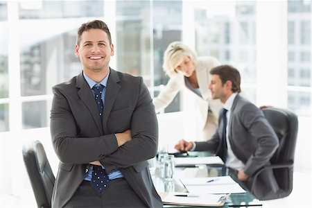 simsearch:400-07274497,k - Portrait of a smiling businessman with colleagues discussing in background at a bright office Stock Photo - Budget Royalty-Free & Subscription, Code: 400-07274494