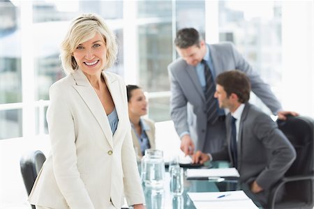 simsearch:400-07274497,k - Portrait of a mature businesswoman with colleagues discussing in background at a bright office Stock Photo - Budget Royalty-Free & Subscription, Code: 400-07274490