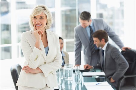 simsearch:400-07274497,k - Portrait of a mature businesswoman with colleagues discussing in background at a bright office Stock Photo - Budget Royalty-Free & Subscription, Code: 400-07274491