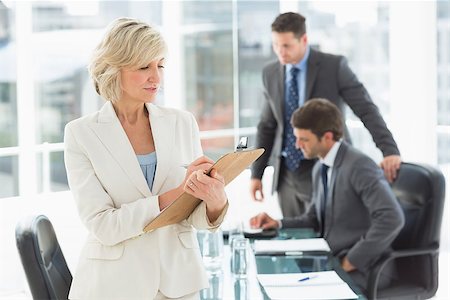 simsearch:400-07274497,k - Mature businesswoman writing on clipboard with colleagues discussing in background at a bright office Stock Photo - Budget Royalty-Free & Subscription, Code: 400-07274492