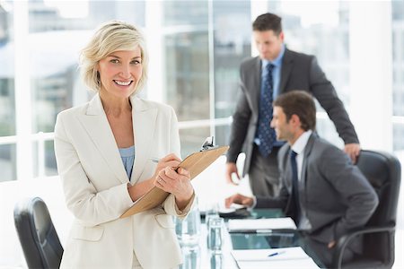simsearch:400-07274497,k - Mature businesswoman writing on clipboard with colleagues discussing in background at a bright office Stock Photo - Budget Royalty-Free & Subscription, Code: 400-07274493