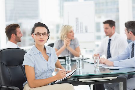 simsearch:400-07274497,k - Young businesswoman holding clipboard with colleagues discussing in background at a bright office Stock Photo - Budget Royalty-Free & Subscription, Code: 400-07274577