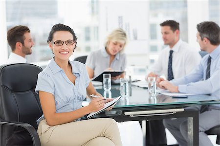 simsearch:400-07274497,k - Young businesswoman holding clipboard with colleagues discussing in background at a bright office Stock Photo - Budget Royalty-Free & Subscription, Code: 400-07274578