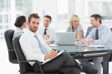 simsearch:400-07274497,k - Young businessman with colleagues discussing in background at a bright office Stock Photo - Budget Royalty-Free & Subscription, Code: 400-07274580