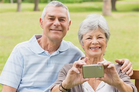 simsearch:400-07274981,k - Cheerful senior couple photographing themselves while sitting on bench at the park Stock Photo - Budget Royalty-Free & Subscription, Code: 400-07274926