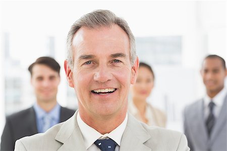 simsearch:400-07274497,k - Mature businessman smiling at camera with team behind him in the office Stock Photo - Budget Royalty-Free & Subscription, Code: 400-07275357