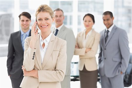 simsearch:400-06879270,k - Businesswoman on the phone smiling at camera with team behind her in the office Stock Photo - Budget Royalty-Free & Subscription, Code: 400-07275363