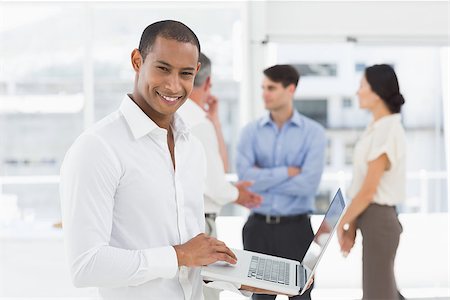 simsearch:400-07274497,k - Young businessman using laptop with team behind him smiling at camera in the office Stock Photo - Budget Royalty-Free & Subscription, Code: 400-07275376