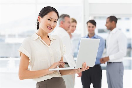 simsearch:400-07275394,k - Smiling asian businesswoman using laptop with team behind her in the office Stock Photo - Budget Royalty-Free & Subscription, Code: 400-07275373