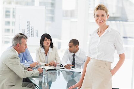 simsearch:400-07275394,k - Happy businesswoman looking at camera while staff discuss behind her in the office Stock Photo - Budget Royalty-Free & Subscription, Code: 400-07275449
