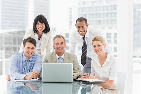 simsearch:400-07275394,k - Happy business people gathered around laptop looking at camera in the office Stock Photo - Budget Royalty-Free & Subscription, Code: 400-07275455