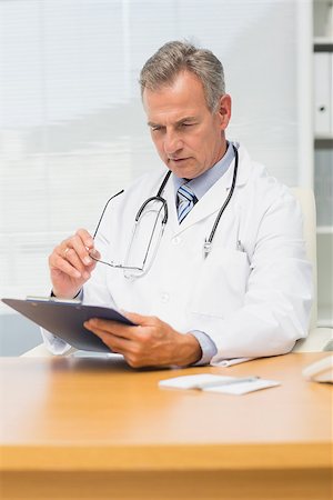 simsearch:614-06898452,k - Concentrating mature doctor sitting at his desk with clipboard in his office at the hospital Stock Photo - Budget Royalty-Free & Subscription, Code: 400-07275586