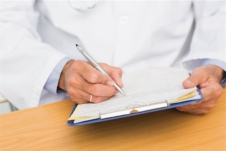 simsearch:614-06898452,k - Doctor sitting at his desk writing on clipboard in his office at the hospital Stock Photo - Budget Royalty-Free & Subscription, Code: 400-07275590
