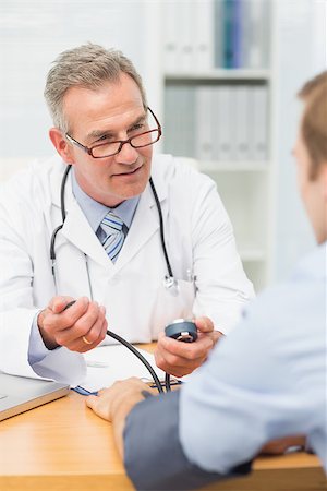 Smiling mature doctor taking his patients blood pressure in his office at the hospital Stock Photo - Budget Royalty-Free & Subscription, Code: 400-07275629