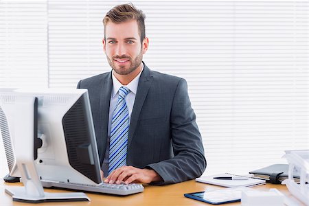 simsearch:400-07272682,k - Portrait of a smiling young businessman using computer at office desk Stockbilder - Microstock & Abonnement, Bildnummer: 400-07275640