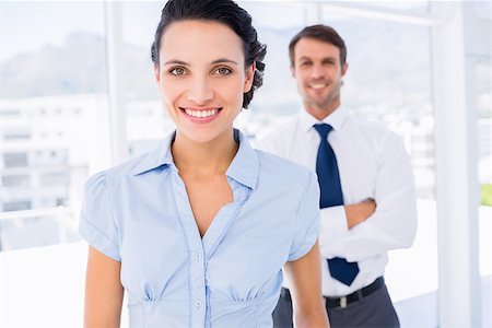 simsearch:400-07275828,k - Portrait of a smiling young businesswoman with male colleague in background at a bright office Photographie de stock - Aubaine LD & Abonnement, Code: 400-07275829