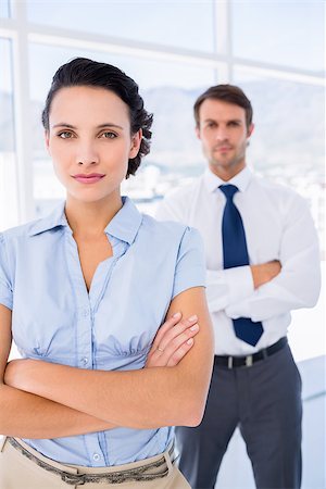 simsearch:400-07275828,k - Portrait of a serious young businesswoman with male colleague in background at a bright office Photographie de stock - Aubaine LD & Abonnement, Code: 400-07275834