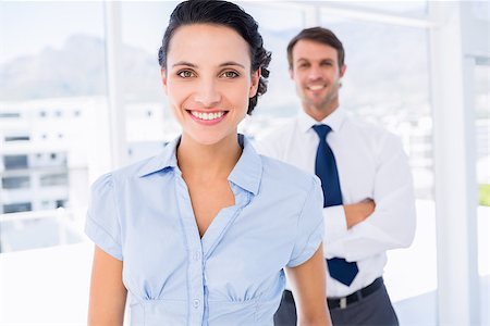 simsearch:400-07275828,k - Portrait of a smiling young businesswoman with male colleague in background at a bright office Photographie de stock - Aubaine LD & Abonnement, Code: 400-07275830