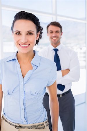 simsearch:400-07275828,k - Portrait of a smiling young businesswoman with male colleague in background at a bright office Photographie de stock - Aubaine LD & Abonnement, Code: 400-07275831