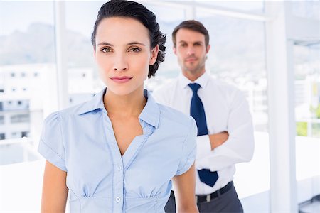 simsearch:400-07275828,k - Portrait of a serious young businesswoman with male colleague in background at a bright office Photographie de stock - Aubaine LD & Abonnement, Code: 400-07275833
