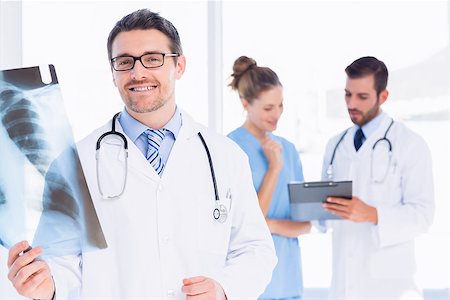 simsearch:400-07778150,k - Male doctor examining xray with colleagues in the background at medical office Stock Photo - Budget Royalty-Free & Subscription, Code: 400-07275994